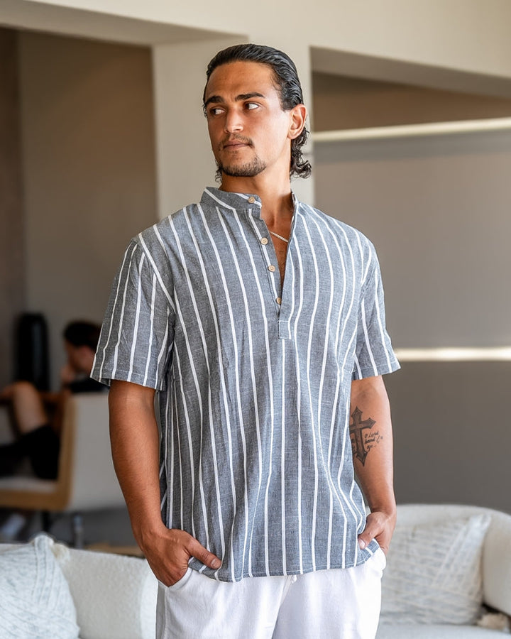 Homme portant la chemise d’été moderne Lyam en lin gris à fines rayures blanches, avec col officier et manches courtes, dans un style élégant et décontracté pour la saison estivale.
