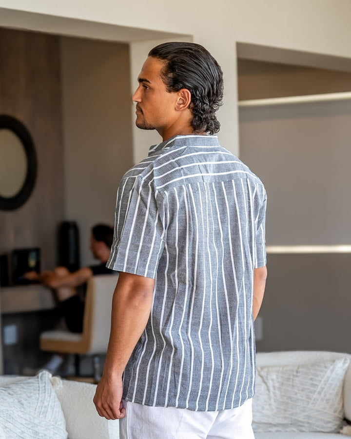Homme portant la chemise d’été moderne Lyam en lin gris à rayures blanches, vue de dos dans un intérieur élégant, avec manches courtes et coupe légère idéale pour l’été.