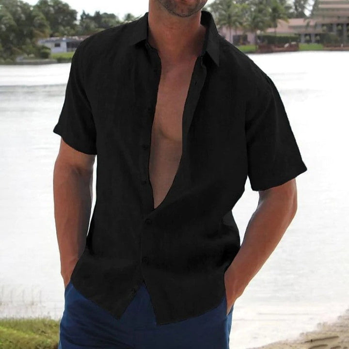 Homme portant la chemise Macon à manches courtes noire, légère et tendance, ouverte sur le devant, idéale pour un style estival décontracté au bord de l’eau.