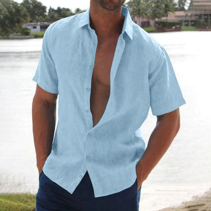 Homme portant la chemise Macon à manches courtes bleu clair, légère et tendance, ouverte sur le devant, parfaite pour un look estival décontracté au bord de l’eau.