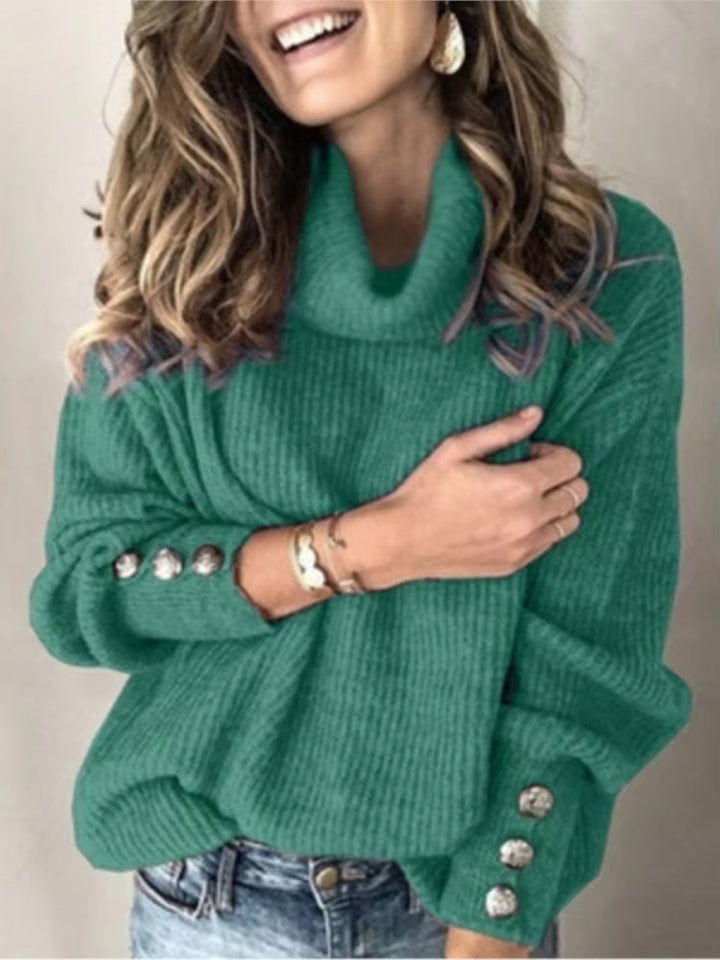 Femme portant un pull à col roulé ample de couleur vert émeraude, décoré de boutons argentés sur les manches. Le tissu en maille épaisse donne un effet doux et confortable, parfait pour un style élégant, moderne et chaleureux durant la saison froide.