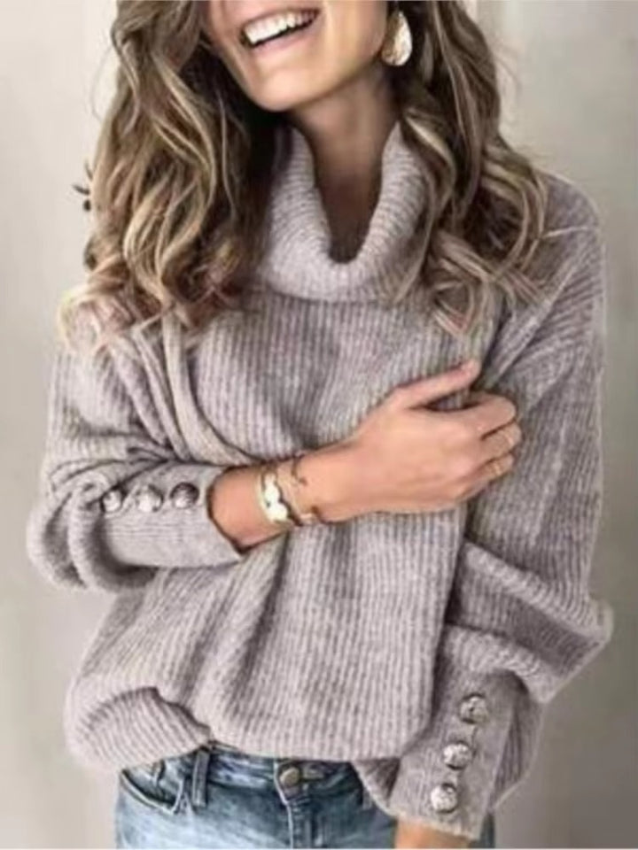 Femme portant un pull gris à col roulé ample, orné de boutons argentés aux manches. La grosse maille lui confère une allure douce et élégante, idéale pour un style confortable et décontracté en automne ou en hiver.