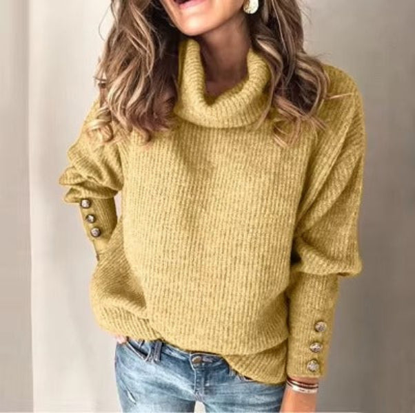 Femme portant un pull à col roulé ample de couleur moutarde, orné de boutons argentés sur les manches. Le tissu en maille douce offre une texture confortable et élégante, idéale pour un look automnal tendance et chaleureux.