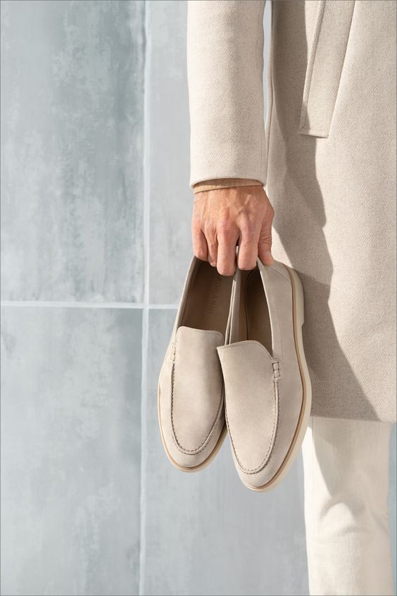 Mocassins en daim beige de haute qualité, tenus dans une main, avec un look moderne et raffiné, parfaits pour un style élégant et contemporain.
