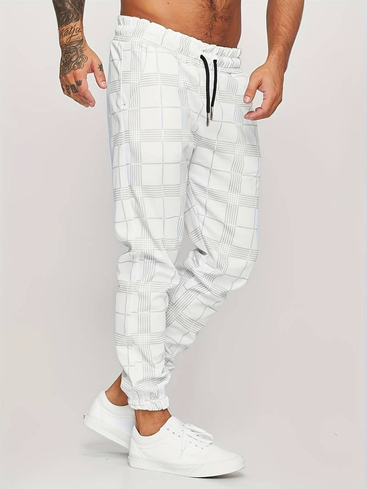 Pantalon de jogging pour homme blanc avec motif à carreaux discrets, coupe moderne et ajustée, taille élastique avec cordon de serrage noir, poches latérales, chevilles resserrées, vue de profil, porté avec des baskets blanches sur fond clair.