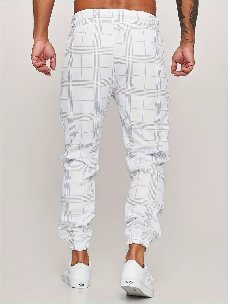 Pantalon de jogging pour homme blanc avec motif à carreaux discrets, coupe moderne et ajustée, taille élastique, chevilles resserrées, vue arrière du bas du dos jusqu’aux pieds, porté avec des baskets blanches sur fond clair.
