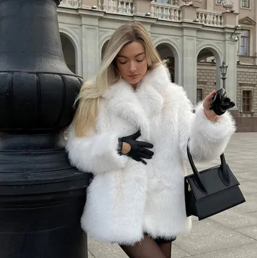  Manteau en fausse fourrure blanche porté avec élégance, associé à des gants noirs et un sac à main chic, idéal pour affronter l’hiver avec style et confort.