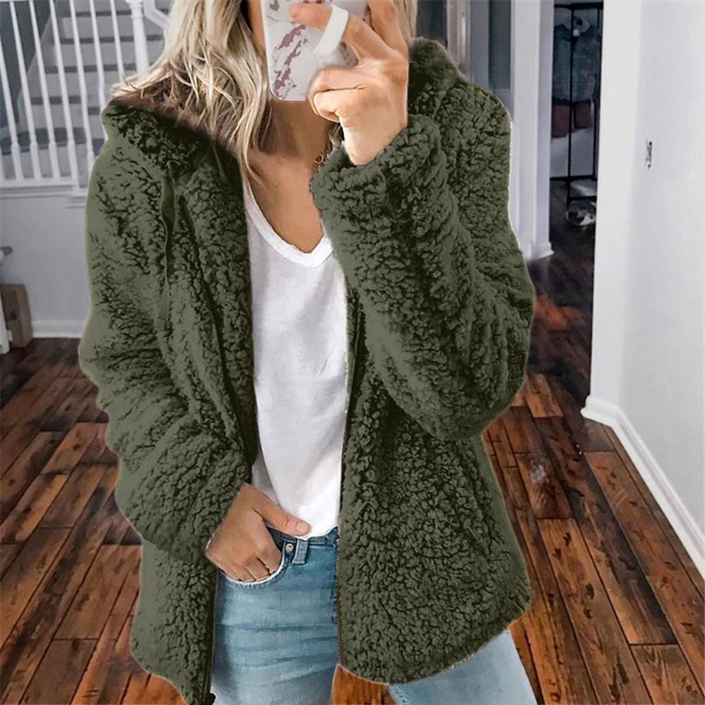 Femme portant la veste d’hiver courte Marie en fausse fourrure chaude, couleur kaki, associée à un t-shirt blanc et un jean, pour un look tendance et décontracté.