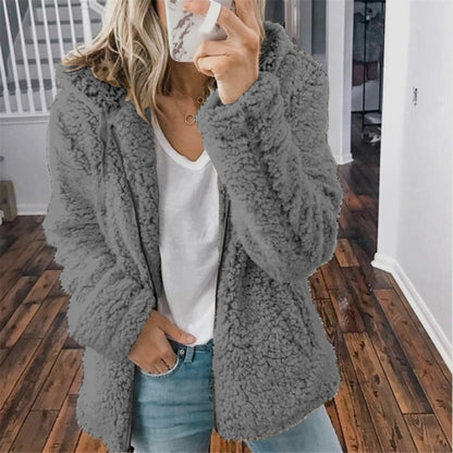 Femme portant la veste d’hiver courte Marie en fausse fourrure chaude, couleur gris foncé, associée à un t-shirt blanc et un jean, pour un style tendance et confortable.