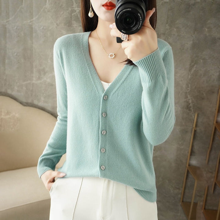 Femme portant un cardigan doux de couleur vert menthe avec col en V et boutons assortis, superposé à un haut blanc et associé à un pantalon clair. Le style épuré et moderne met en valeur une maille fine et une coupe élégante.