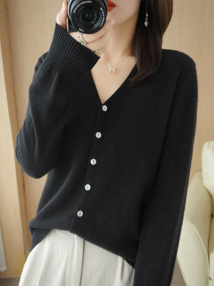 Femme portant un cardigan noir à col en V, doté de boutons contrastés et d’une maille fine, associé à un pantalon clair. Le style minimaliste et moderne met en valeur une coupe élégante et intemporelle.