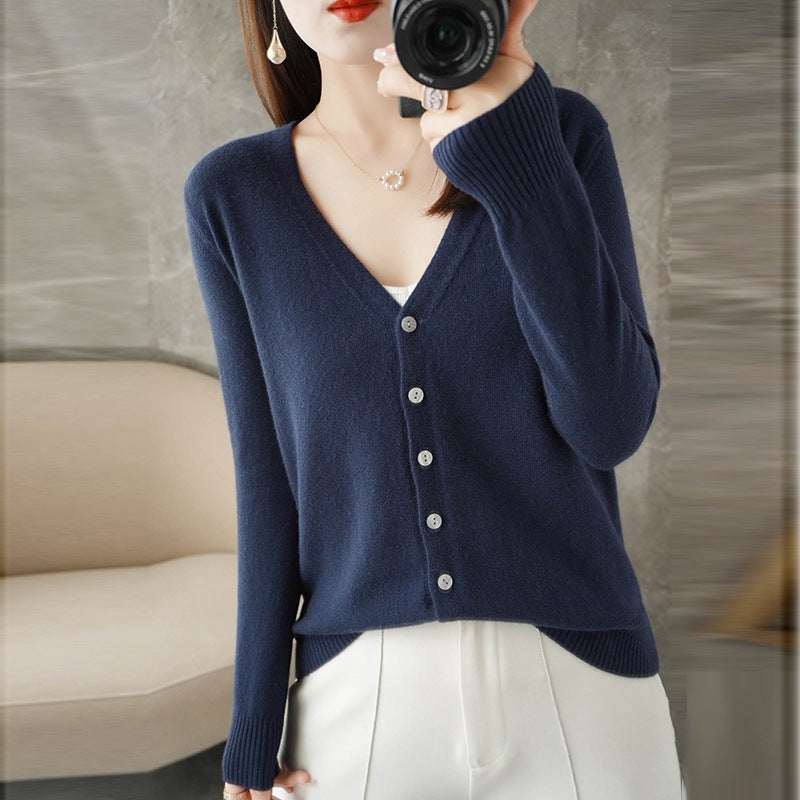 Femme portant un cardigan bleu marine à col en V, doté de boutons assortis et d’une maille fine, superposé à un haut blanc et associé à un pantalon clair. Le style épuré et moderne met en valeur une coupe élégante et féminine.