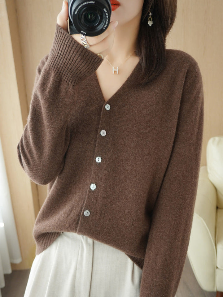Femme portant un cardigan marron à col en V, doté de boutons contrastés et d’une maille fine, associé à un pantalon clair. La coupe simple et moderne met en valeur un style élégant, doux et intemporel.