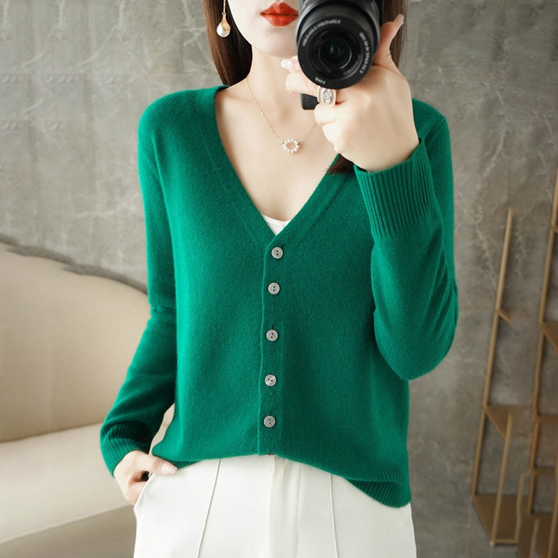 Femme portant un cardigan vert émeraude à col en V, doté de boutons assortis et d’une maille fine, superposé à un haut blanc et associé à un pantalon clair. Le style moderne et épuré met en valeur une coupe élégante et féminine.