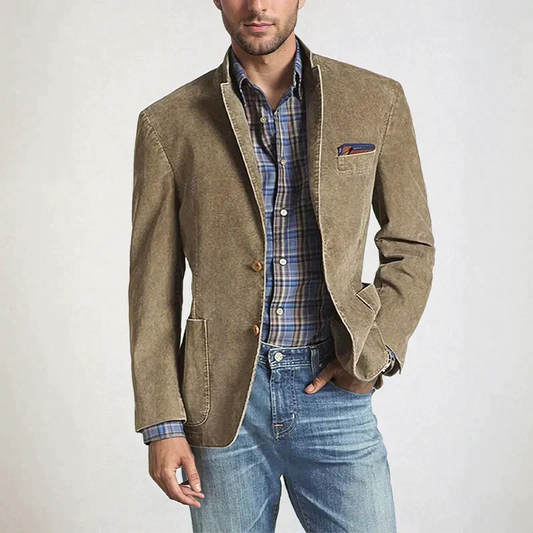 Un homme porte un blazer décontracté de couleur beige, avec une chemise à carreaux bleus et verts sous le blazer. Il est assorti de jeans clairs, et un mouchoir de poche orne la poche supérieure du blazer, offrant un look élégant mais décontracté.