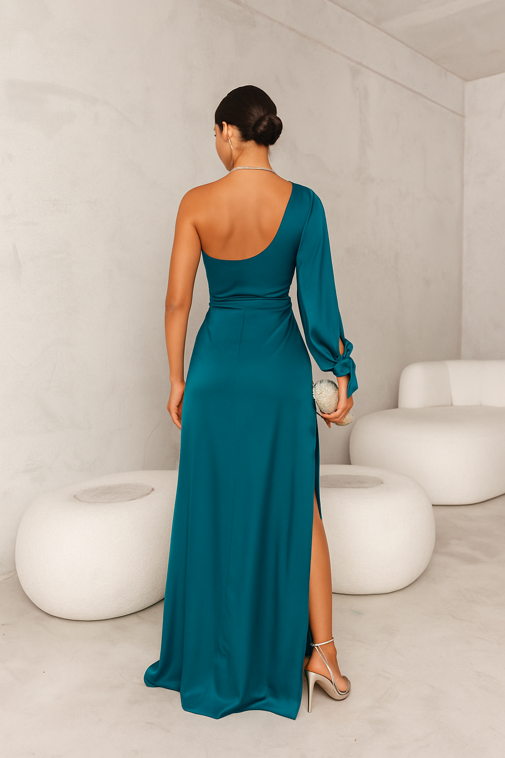 Vue de dos de cette élégante robe en satin turquoise à la coupe asymétrique dévoilant une épaule et ornée d'une ceinture à nouer. La fente latérale apporte une touche de sensualité, tandis que le sac à main argenté et les escarpins assortis complètent cette tenue chic et moderne, idéale pour vos occasions spéciales.
