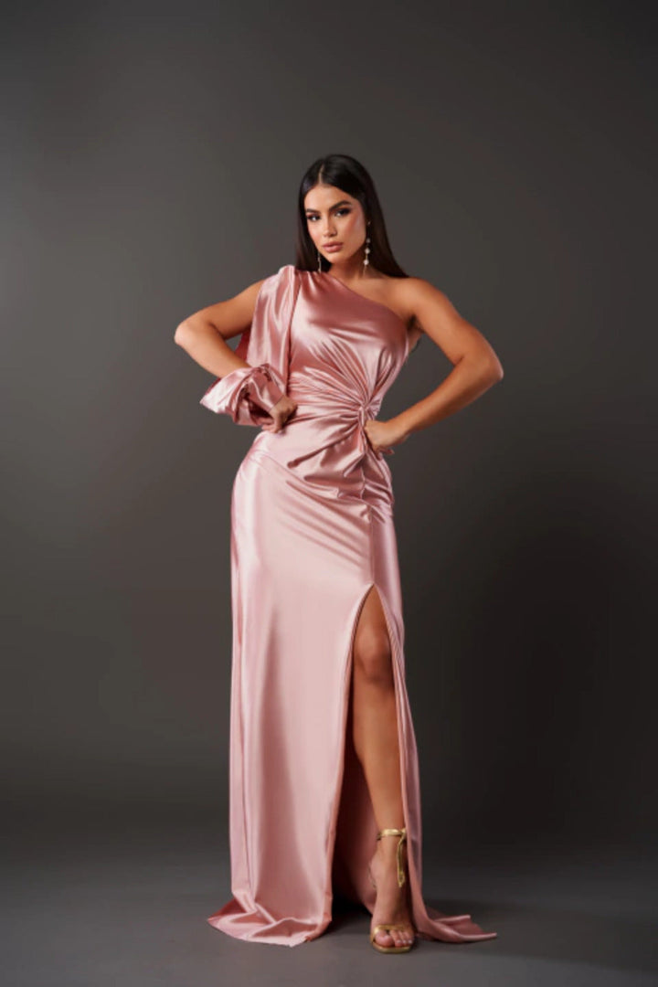 Cette robe rose satinée à épaule unique et détail noué à la taille est parfaite pour des occasions spéciales. Sa coupe élégante et moderne, avec une fente sur le côté, met en valeur la silhouette, tandis que les accessoires dorés et les talons ajoutent une touche de sophistication.