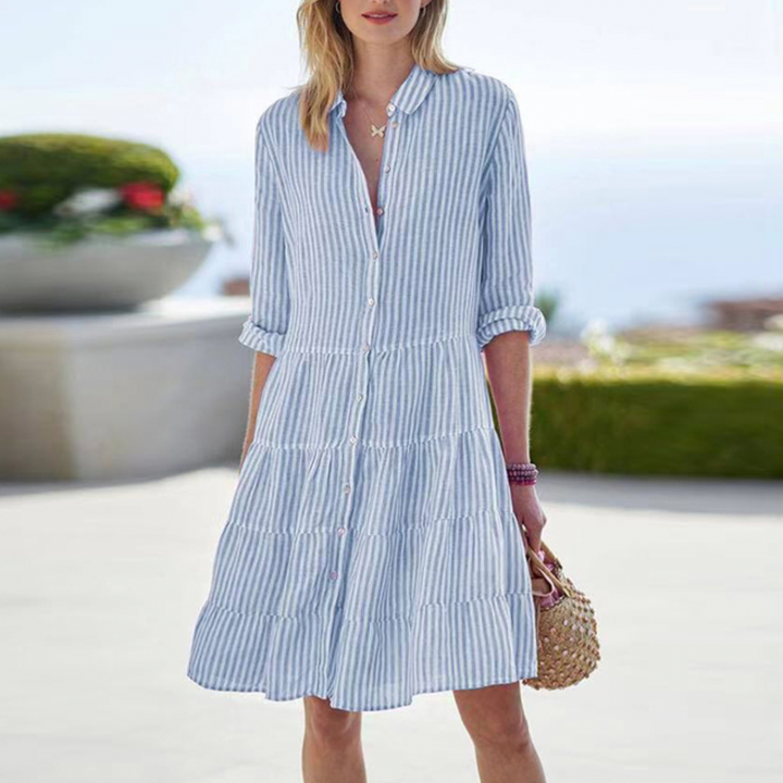 Robe chic pour femme Merton, tendance et élégante, de couleur bleu clair à rayures. Cette robe à manches longues avec des boutons présente une coupe fluide et légère, parfaite pour un look estival décontracté et raffiné. Accessoirisée avec un sac en perles et des bracelets, elle est idéale pour les journées ensoleillées.