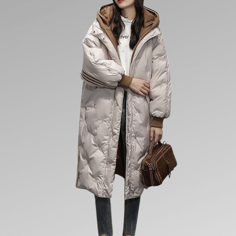 Michelle, doudoune longue beige pour femme avec capuche doublée marron et manches amples, manteau d’hiver chaud et élégant idéal pour affronter le froid avec style.