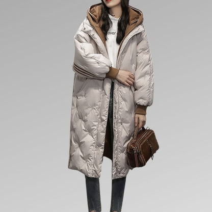 Michelle, doudoune longue beige pour femme avec capuche doublée marron et manches amples, manteau d’hiver chaud et élégant idéal pour affronter le froid avec style.