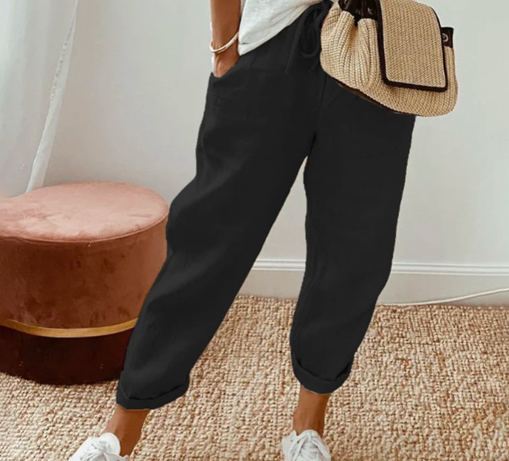 Pantalon ample noir à coupe large, avec taille élastique et cordon de serrage, poches latérales, porté dans un style décontracté avec un haut clair et des baskets blanches, dans un intérieur lumineux et épuré.