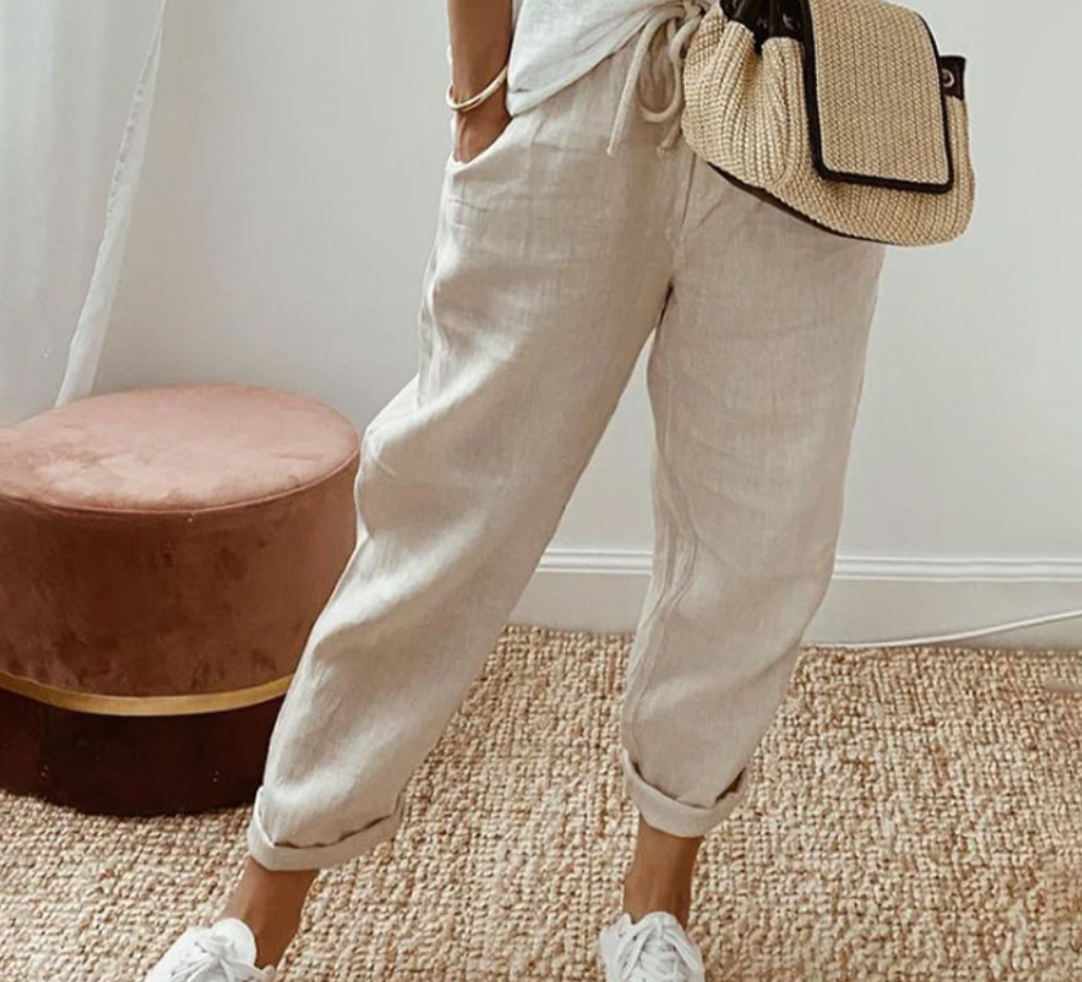 Pantalon ample de couleur beige clair, à coupe large et taille élastique avec cordon de serrage, porté de manière décontractée avec un haut clair et des baskets blanches, dans un intérieur lumineux au style minimaliste.