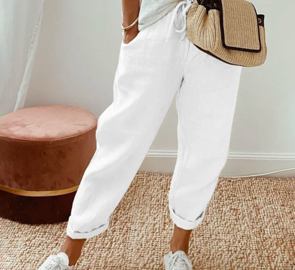 Pantalon ample blanc à coupe large, avec taille élastique et cordon de serrage, poches latérales, porté dans un style décontracté avec un haut clair et des baskets blanches, dans un intérieur lumineux au design minimaliste.