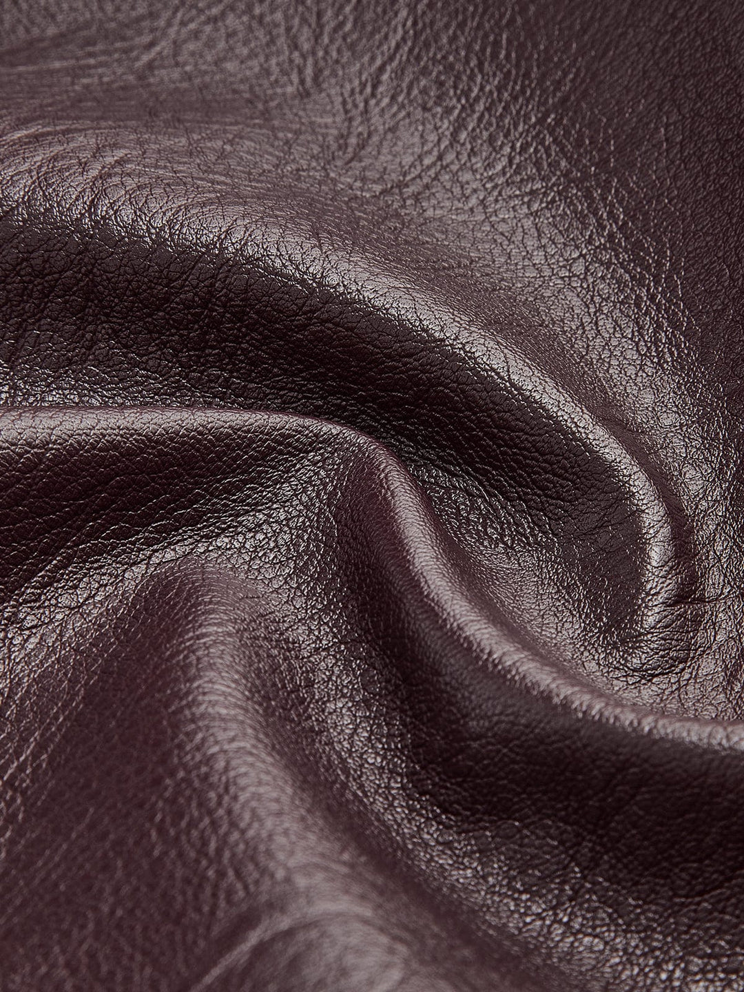 Gros plan sur le tissu en simili cuir bordeaux, mettant en valeur la texture lisse et brillante du matériau, soulignant sa qualité et son aspect moderne.