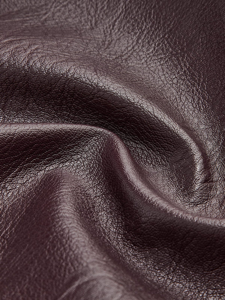 Gros plan sur le tissu en simili cuir bordeaux, mettant en valeur la texture lisse et brillante du matériau, soulignant sa qualité et son aspect moderne.