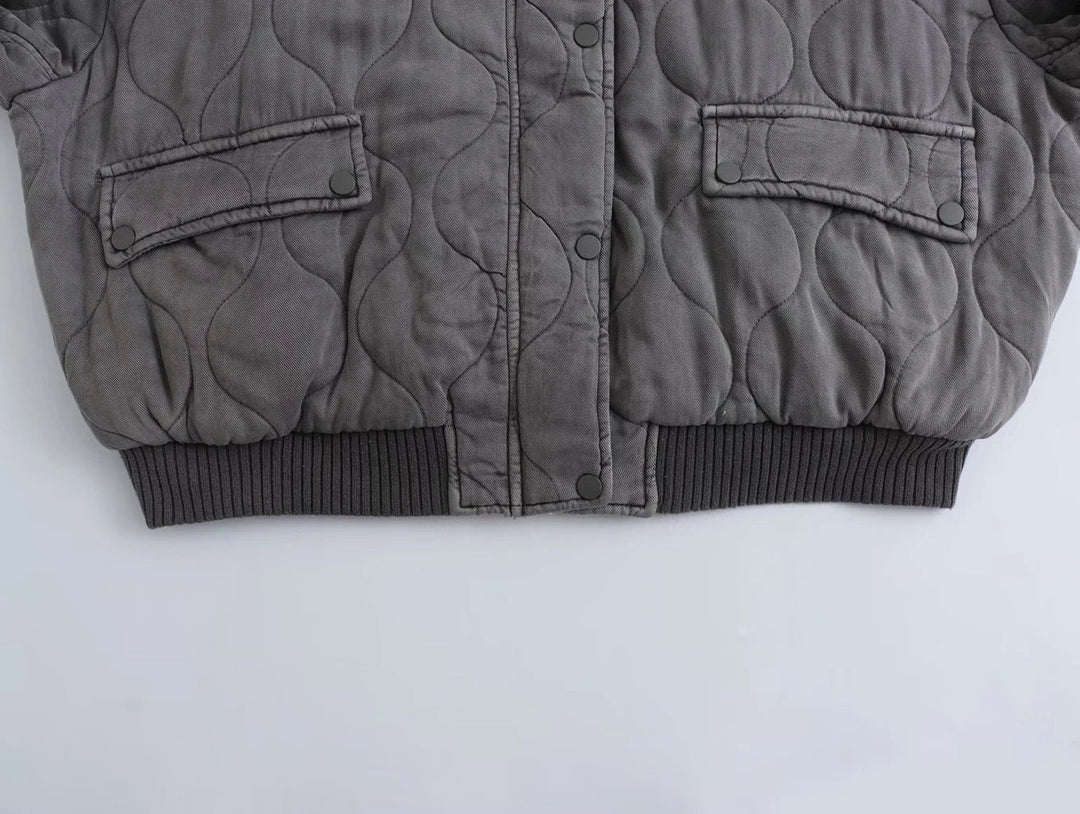 Détail du bas du blouson long pour femme "Nancy" en gris, avec un design matelassé, des poches à rabat et une finition côtelée au niveau de la taille. Parfait pour un look à la fois décontracté et élégant.