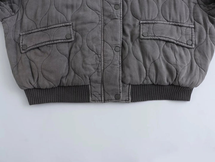 Détail du bas du blouson long pour femme "Nancy" en gris, avec un design matelassé, des poches à rabat et une finition côtelée au niveau de la taille. Parfait pour un look à la fois décontracté et élégant.