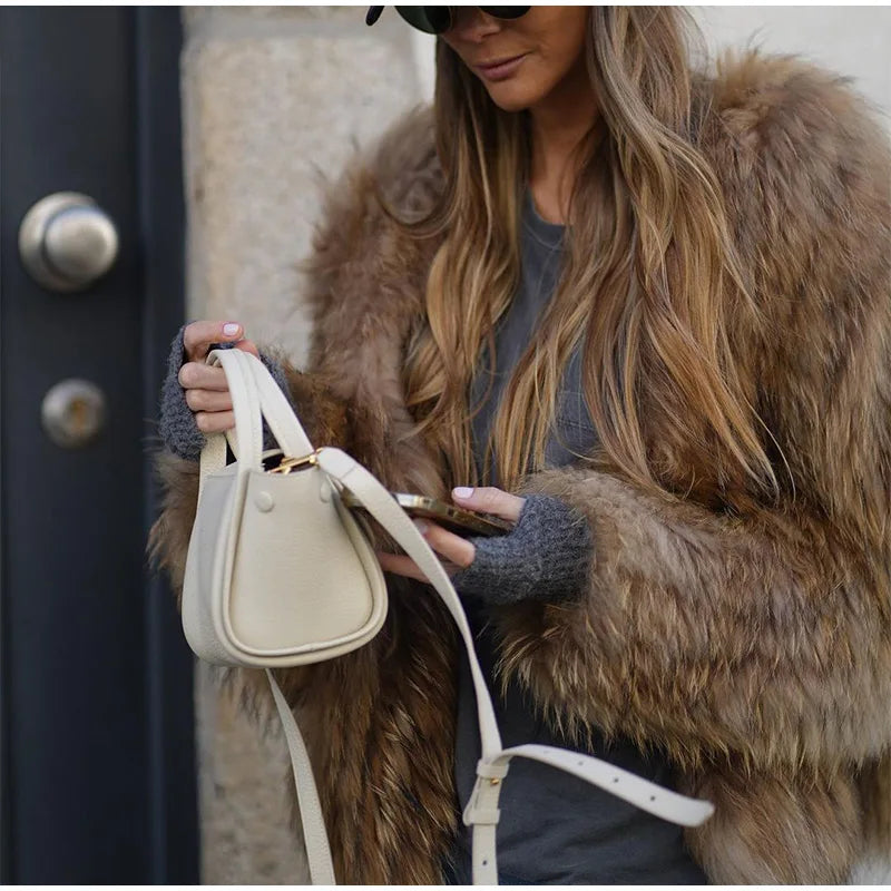 Nicole | Veste longue pour femme en fourrure marron, idéale pour l'hiver, portée avec une petite sacoche blanche et des gants gris, style chic et décontracté.