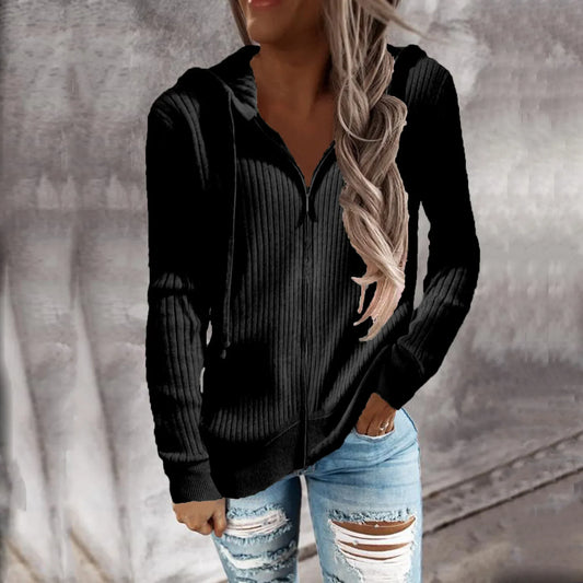 Veste à capuche zippée noire en maille côtelée, portée par une femme avec de longs cheveux. Elle est habillée d'un jean déchiré et adopte un look décontracté, parfait pour les journées fraîches.