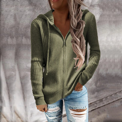 Une femme portant un sweat à capuche zippé de couleur olive. Le sweat présente un motif côtelé et une coupe ajustée, avec des manches longues et un zip sur le devant. Elle le porte avec un jean déchiré pour un look décontracté et stylé.