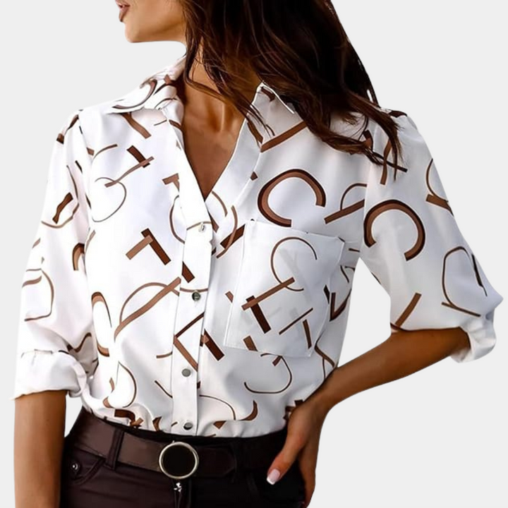 Chemise femme Nivelle blanche à lettres graphiques marron portée avec un pantalon foncé. Modèle élégant avec col classique, poche poitrine et manches retroussées, parfait pour un look tendance et moderne.