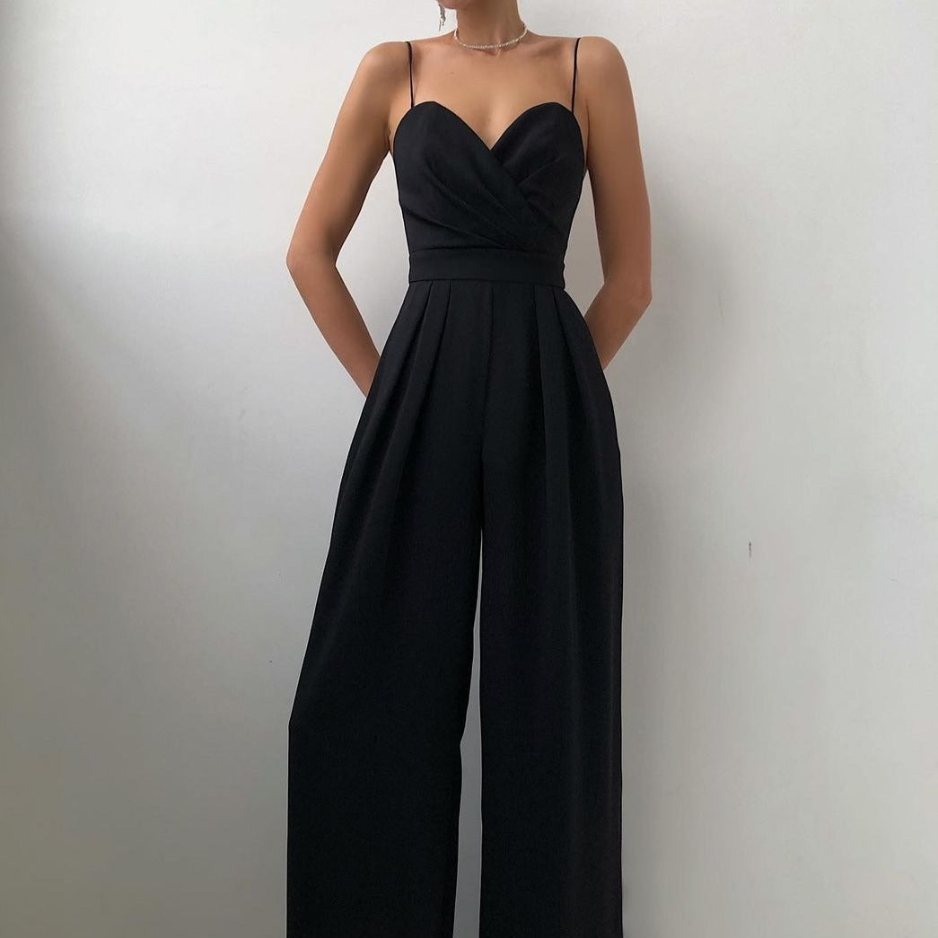 Combinaison longue noire à fines bretelles, décolleté cœur croisé et taille ceinturée, avec pantalon large fluide, portée par un mannequin sur fond gris clair.