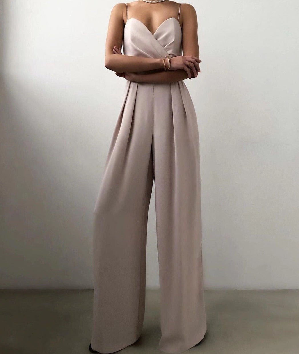 Combinaison longue beige clair à fines bretelles, décolleté cœur croisé et taille marquée, avec pantalon large fluide, portée par un mannequin sur fond neutre.