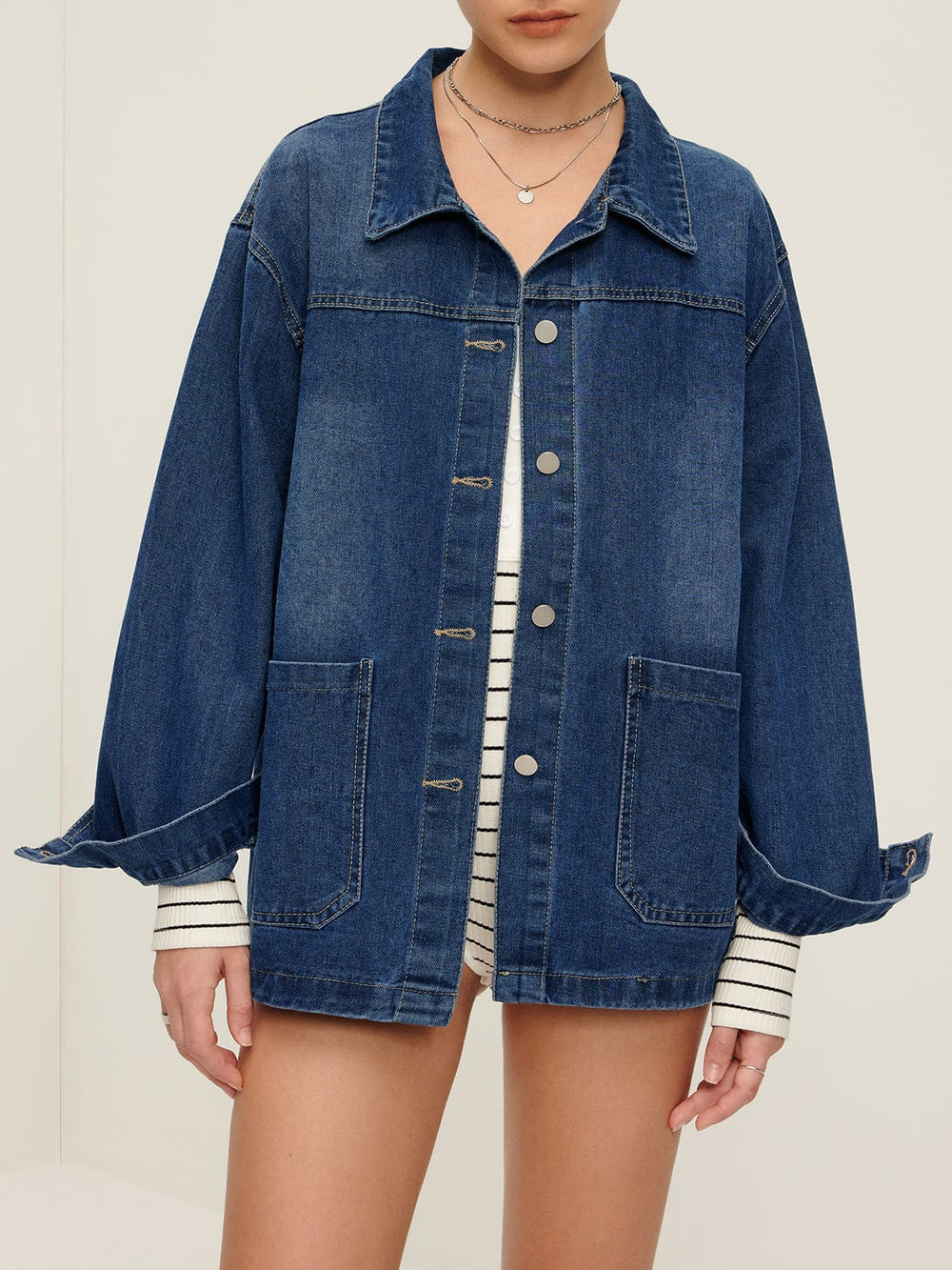 Veste en jean Nyselle pour femme, avec une coupe moderne et décontractée. Le modèle porte la veste à boutons métalliques avec de grandes poches et des manches ballons, créant un look stylé et tendance, parfait pour une tenue casual.
