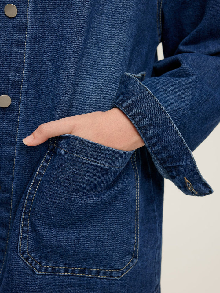 Détail de la veste en jean Nyselle pour femme, montrant la poche avant et le bouton métallique. Ce zoom sur le tissu en denim bleu souligne la coupe moderne et pratique, avec des poches fonctionnelles pour un look à la fois stylé et décontracté.
