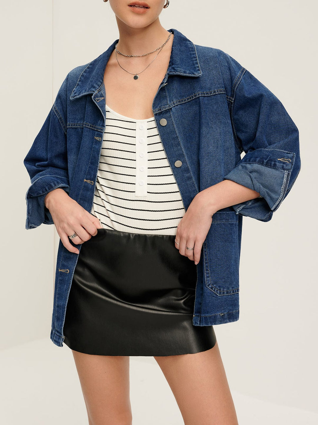 Veste en jean 'Nyselle' pour femme, portée avec une tenue décontractée composée d'un haut à rayures et d'une jupe en simili cuir. La veste en denim bleu est dotée de boutons métalliques et de manches retroussées, offrant un look moderne et stylé, parfait pour un style casual et tendance.