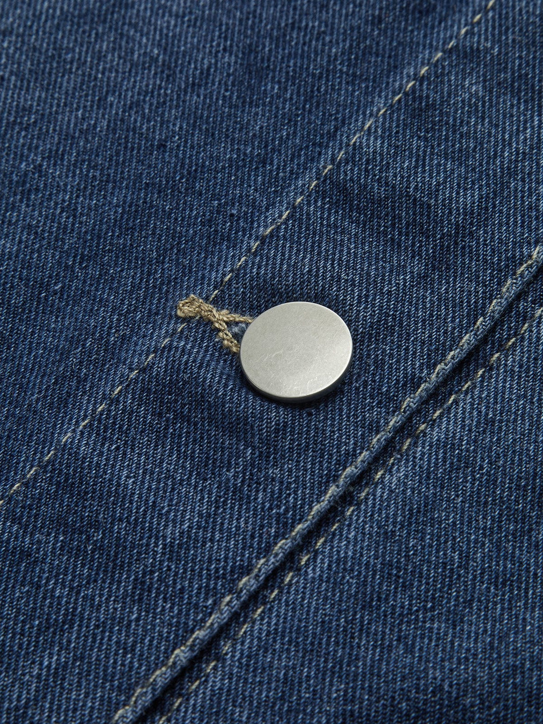 Détail du bouton métallique de la veste en jean 'Nyselle' pour femme, mettant en valeur la qualité du tissu en denim bleu et la finition soignée. Ce zoom sur le bouton montre l'attention portée aux détails, ajoutant une touche moderne à cette veste décontractée.