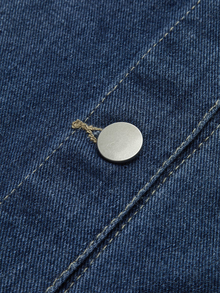Détail du bouton métallique de la veste en jean 'Nyselle' pour femme, mettant en valeur la qualité du tissu en denim bleu et la finition soignée. Ce zoom sur le bouton montre l'attention portée aux détails, ajoutant une touche moderne à cette veste décontractée.
