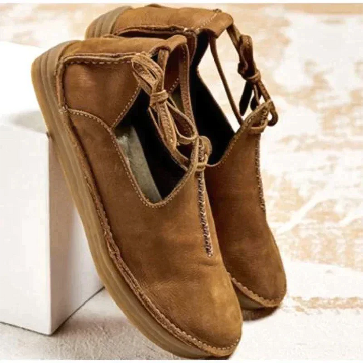 Chaussures d’automne pour femme en cuir marron camel, au style moderne et naturel, avec coutures artisanales apparentes, lien décoratif sur le côté, ouverture souple et semelle plate confortable, présentées sur un fond clair.