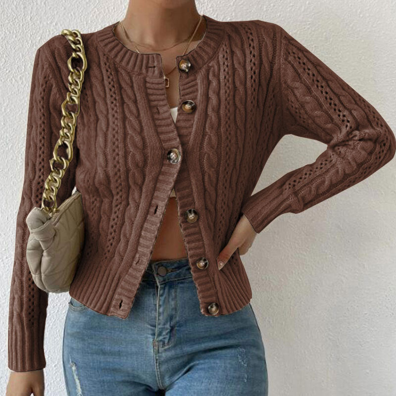 Femme portant un cardigan texturé marron à motifs torsadés, légèrement ouvert sur un haut blanc et assorti à un jean taille haute. Le modèle met en valeur une maille détaillée, des boutons décoratifs et une coupe moderne et élégante, complétée par un sac à chaîne dorée.