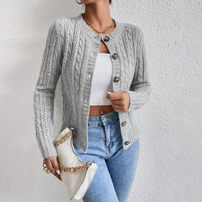 Femme portant un cardigan texturé gris à motifs torsadés, légèrement ouvert sur un haut court blanc et assorti à un jean taille haute. Le modèle met en valeur une maille détaillée, des boutons décoratifs et une coupe moderne et élégante, accompagné d’une pochette blanche à chaîne dorée.