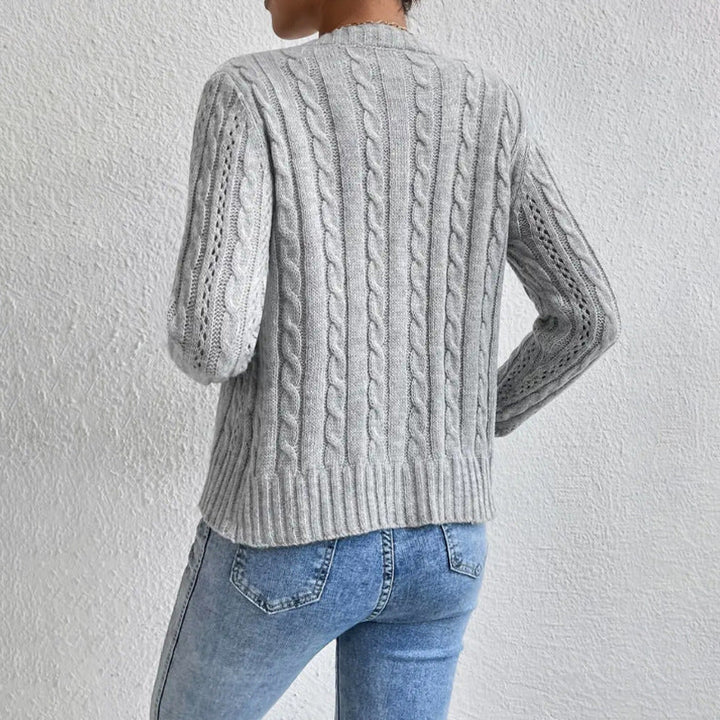 Vue arrière d’un cardigan texturé gris pour femme, mettant en valeur des motifs torsadés verticaux et une finition côtelée au bas. Le vêtement est porté avec un jean taille haute, offrant un style moderne, doux et élégant.