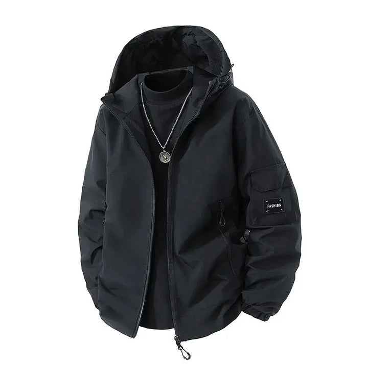 Veste d'hiver pour homme de couleur noire avec capuche. Cette veste moderne est dotée de poches zippées sur les côtés et d’un logo sur la manche. Idéale pour les journées fraîches, avec un style casual et pratique.