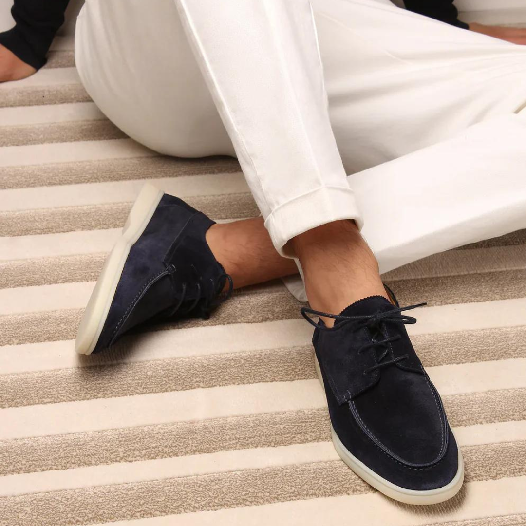 Homme portant les mocassins à lacets Paulin en suédine bleu marine avec semelle blanche contrastante, associés à un pantalon blanc pour un style élégant, moderne et décontracté.