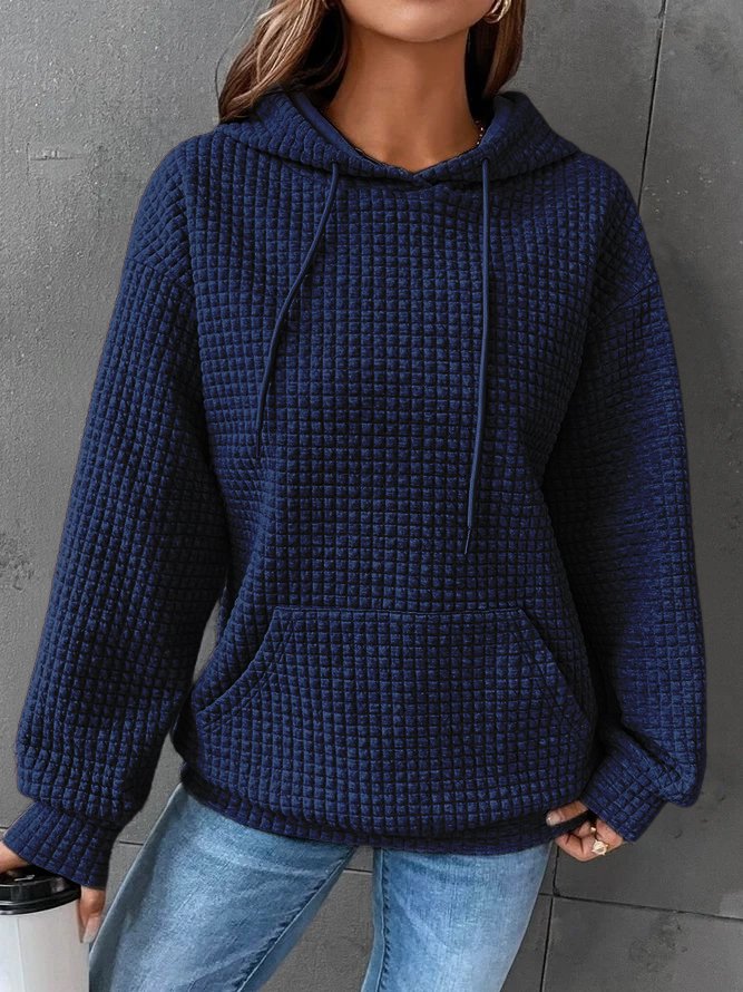 Une femme porte un sweat à capuche bleu en maille gaufrée, doté d'une grande poche kangourou et de cordons de serrage assortis. Sa coupe ample et décontractée est idéale pour un style moderne et confortable. Son tissu épais et chaud en fait une pièce parfaite pour l'hiver. Le fond gris met en valeur la couleur profonde et la texture structurée du sweat.