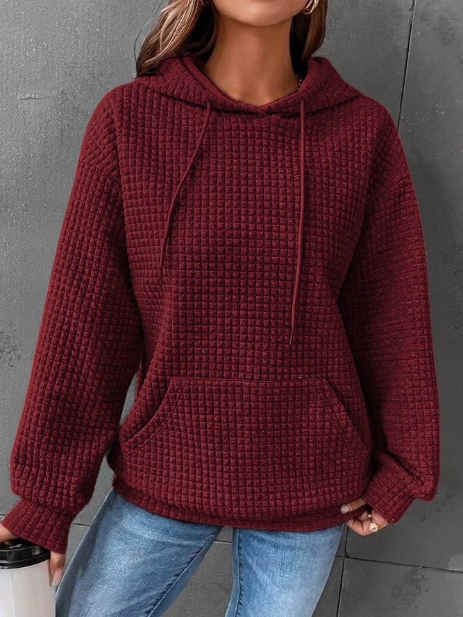 Une femme porte un sweat à capuche rouge à texture gaufrée, doté d'une grande poche kangourou et de cordons de serrage assortis. Sa coupe ample et décontractée lui confère un style moderne et confortable. Le tissu épais et doux procure une sensation de chaleur idéale pour l'hiver. Le fond gris met en valeur la couleur intense du sweat et la texture détaillée du tissu.